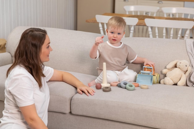 Família feliz em casa Mãe e bebê brincando com brinquedos no sofá em casa dentro de casa Criança pequena e babá se divertindo juntos Jovem mãe mãe filho descansa na sala de estar