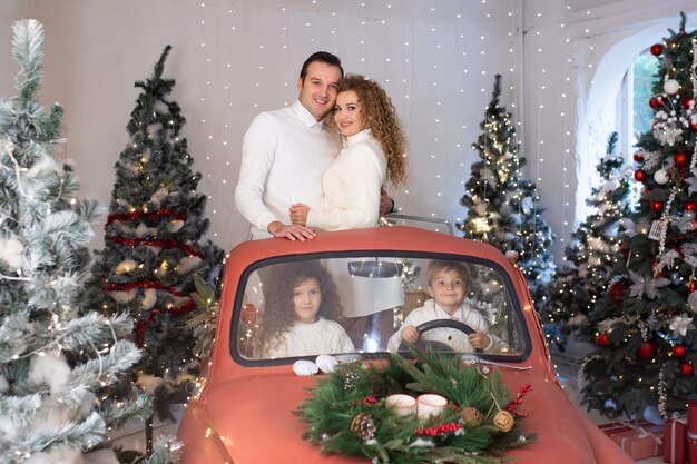 Foto família feliz em um carro vermelho perto de árvores de natal. aproveitando o tempo juntos nas férias.