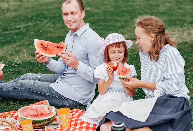 Família feliz em um piquenique comendo melancia Mãe pai e filho em um piquenique no prado ou parque