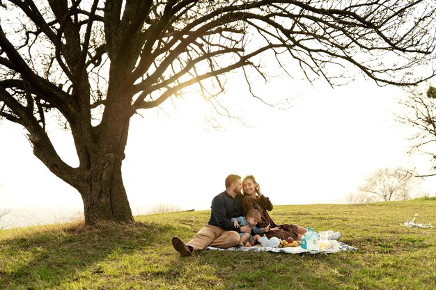 Família feliz em um piquenique um pai com uma esposa grávida e uma filha pequena estão na natureza no parque ao pôr do sol família jovem está descansando no gramado comida e bebidas para um piquenique casal positivo