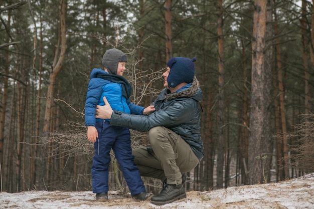 Família feliz em uma caminhada ao ar livre na floresta ensolarada de inverno, férias de Natal, pai e filho brincam juntos