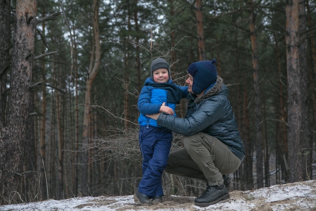 Família feliz em uma caminhada ao ar livre na floresta ensolarada de inverno, férias de Natal, pai e filho brincam juntos