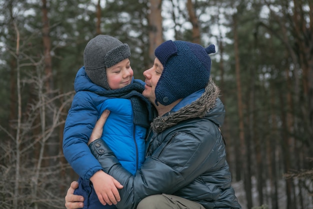 Família feliz em uma caminhada ao ar livre na floresta ensolarada de inverno, férias de Natal, pai e filho brincam juntos