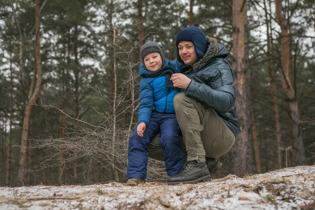 Família feliz em uma caminhada ao ar livre na floresta ensolarada de inverno, férias de Natal, pai e filho brincam juntos