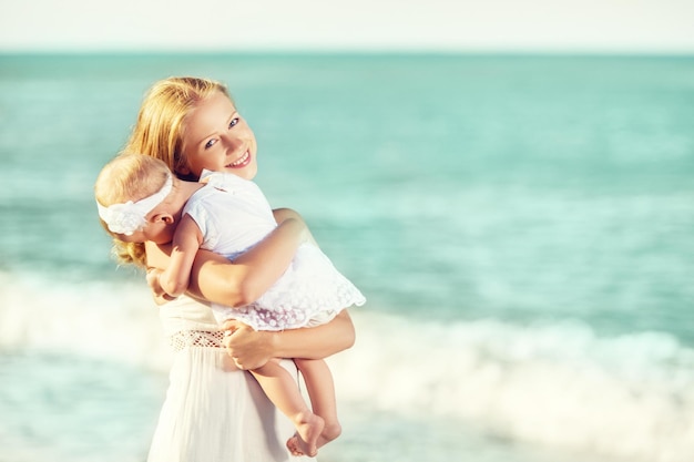 Família feliz em vestido branco mãe abraça bebê no céu na praia