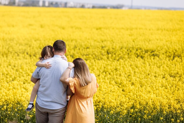 Familia feliz embarazada con hija pequeña pasar tiempo juntos en un campo de colza amarillo en verano