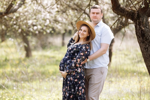 Foto familia feliz. esposa embarazada y su esposo se abrazan en el parque floreciente de la primavera.