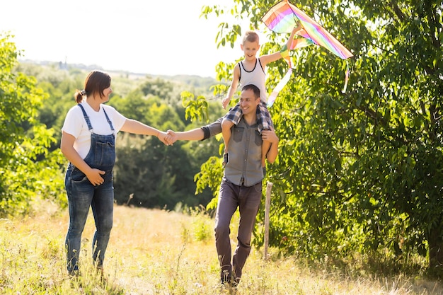 Familia feliz con esposa embarazada volar una cometa juntos en el campo de verano