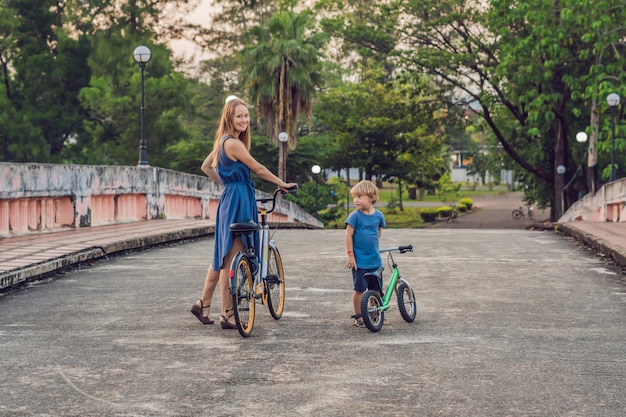 Família feliz está andando de bicicleta ao ar livre e sorrindo. Mãe em uma bicicleta e filho em uma bicicleta equilibrada