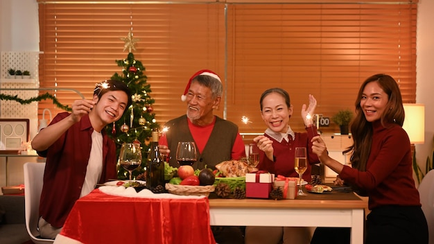 La familia feliz está cenando en casa celebrando la fiesta de Navidad o Año Nuevo con bengalas