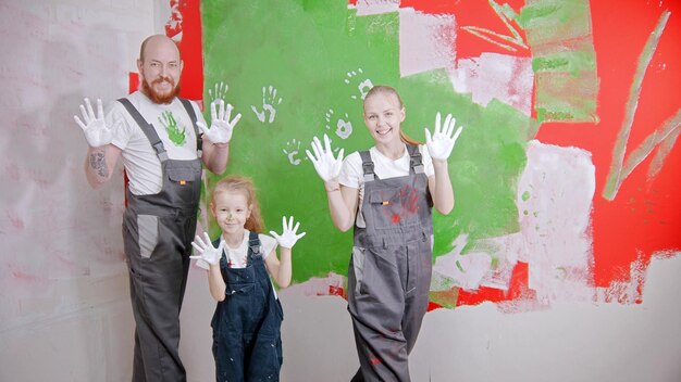 Família feliz está colocando suas impressões brancas em uma parede verde olhando para a câmera