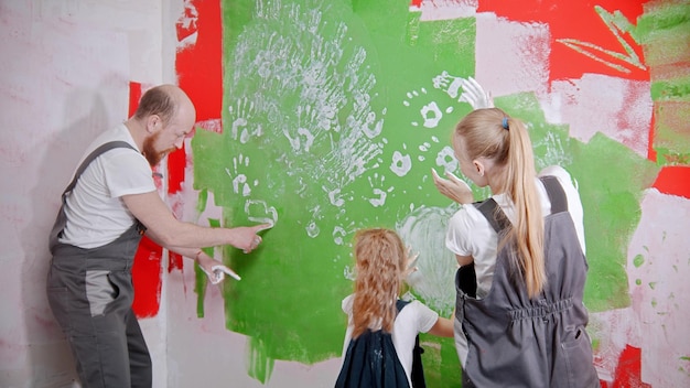 Família feliz está colocando suas impressões brancas em uma parede verde, pai desenhando algo na parede