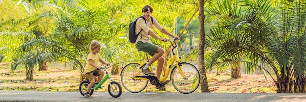 La familia feliz está montando en bicicleta al aire libre y el padre sonriente en una bicicleta y el hijo en una pancarta de balancebike