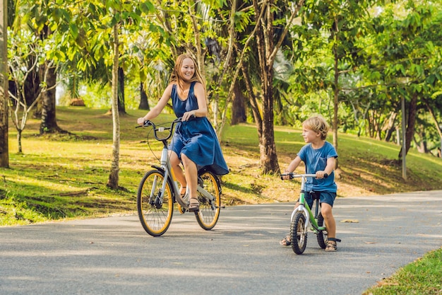 La familia feliz está montando bicicleta al aire libre y sonriendo. Mamá en bicicleta e hijo en bicicleta de equilibrio.