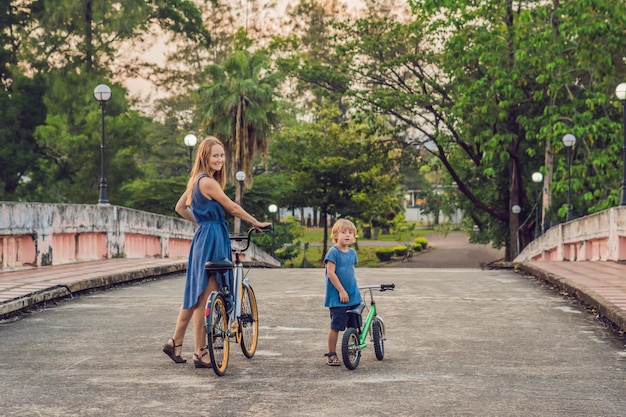 La familia feliz está montando bicicleta al aire libre y sonriendo. Mamá en bicicleta e hijo en bicicleta de equilibrio.