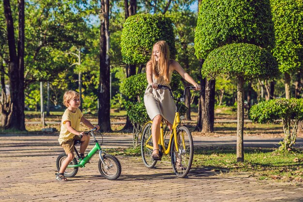 La familia feliz está montando bicicleta al aire libre y sonriendo. Mamá en bicicleta e hijo en bicicleta de equilibrio.