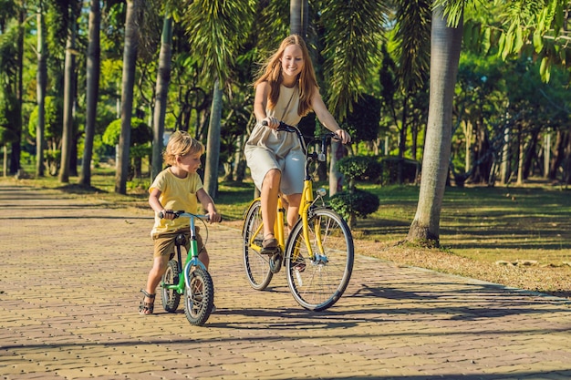 La familia feliz está montando bicicleta al aire libre y sonriendo. Mamá en bicicleta e hijo en bicicleta de equilibrio.