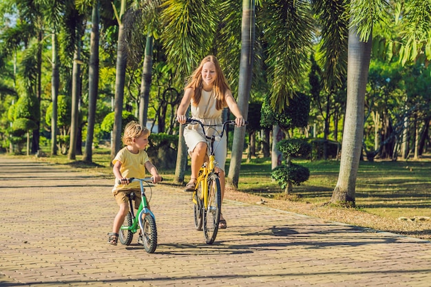 La familia feliz está montando bicicleta al aire libre y sonriendo. Mamá en bicicleta e hijo en bicicleta sin pedales.