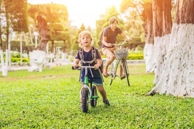 La familia feliz está montando bicicleta al aire libre y sonriendo. Padre en bicicleta e hijo en bicicleta de equilibrio.
