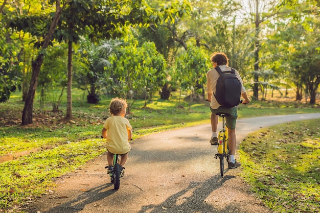 La familia feliz está montando bicicleta al aire libre y sonriendo. Padre en bicicleta e hijo en bicicleta de equilibrio