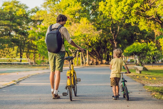 La familia feliz está montando bicicleta al aire libre y sonriendo. Padre en bicicleta e hijo en bicicleta de equilibrio