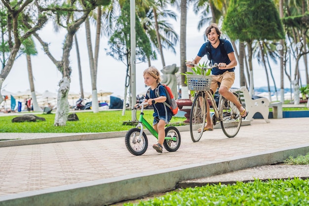 La familia feliz está montando bicicleta al aire libre y sonriendo. Padre en bicicleta e hijo en bicicleta de equilibrio