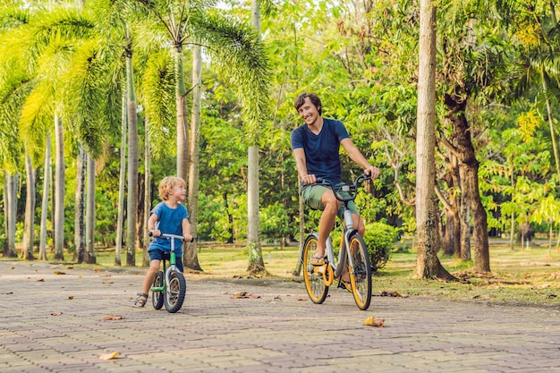 La familia feliz está montando bicicleta al aire libre y sonriendo. Padre en bicicleta e hijo en bicicleta de equilibrio