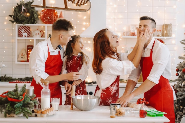 Una familia feliz está de pie en la cocina navideña y se unta con harina.