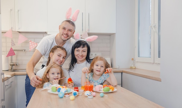 Una familia feliz se está preparando para Pascua pintando huevos de Pascua en la cocina