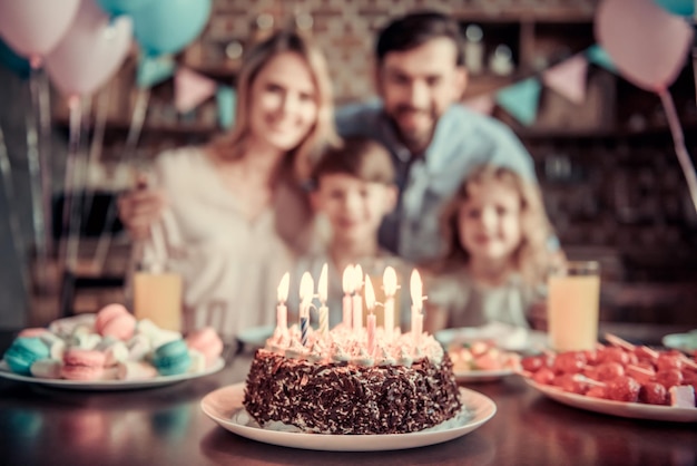 La familia feliz está sentada a la mesa en la cocina decorada durante la celebración del cumpleaños, pastel de cumpleaños en primer plano