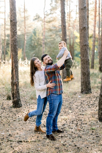 Familia feliz con estilo en ropa casual, papá, mamá e hijo pequeño están caminando en el bosque de otoño, divirtiéndose y jugando con el bebé