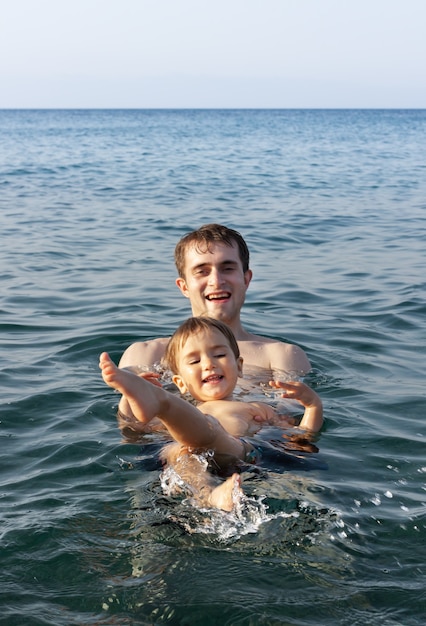 Familia feliz y estilo de vida saludable. Un padre joven enseña a un niño a nadar en el mar.