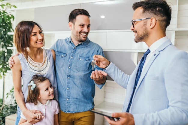 Família feliz falando uma chave de sua nova casa com agente imobiliário.