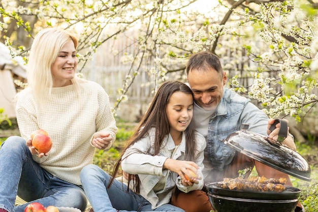 Família feliz fazendo churrasco com churrasqueira moderna ao ar livre.