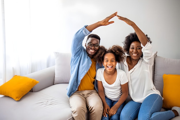 Família feliz formando telhado de casa com as mãos em casa Conceito de seguro