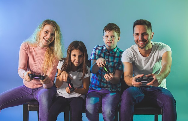 Familia feliz con gamepads jugando videojuegos sobre fondo azul Concepto de entretenimiento y juegos familiares