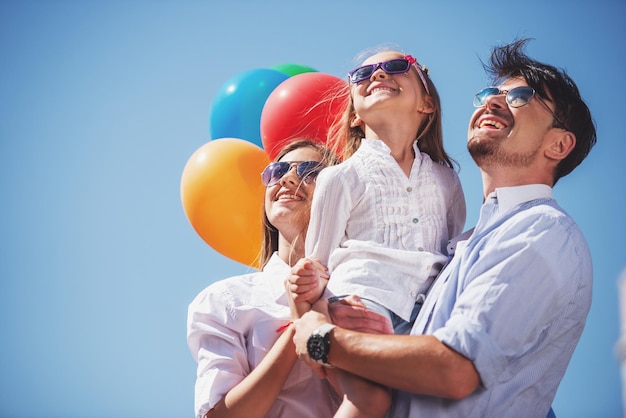 Familia feliz con globos mirando hacia arriba al aire libre en un día de verano.