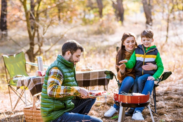 Família feliz grelhando carne na churrasqueira no parque outono