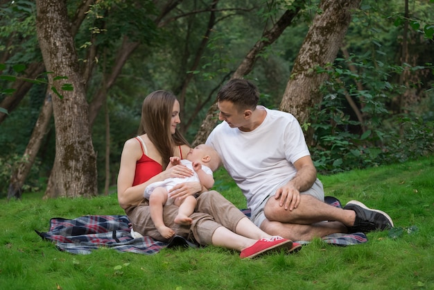 Familia feliz hacer un picnic al aire libre. Joven mamá papá y bebé recién nacido sentado en una manta de picnic.