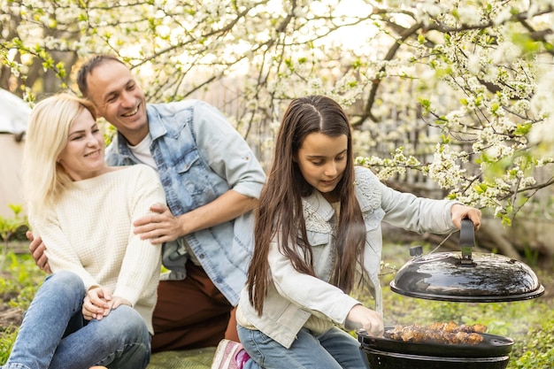 Familia feliz haciendo una barbacoa en su jardín en primavera. Concepto de ocio, comida, familia y vacaciones.