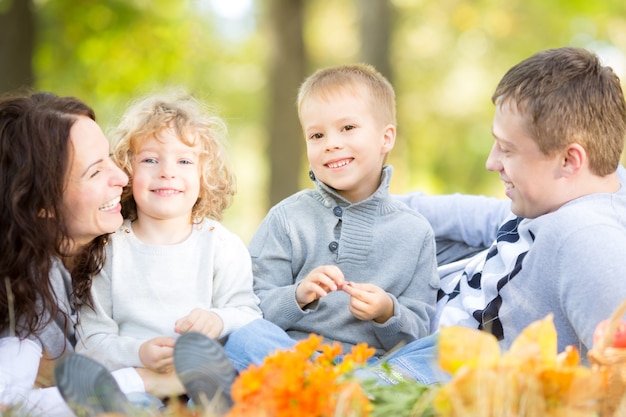 Familia feliz haciendo un picnic al aire libre en el parque de otoño contra el fondo de hojas borrosas