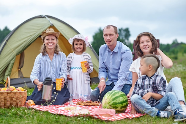 Familia feliz haciendo un picnic en el prado en un día soleado Familia disfrutando de vacaciones de camping en el campo