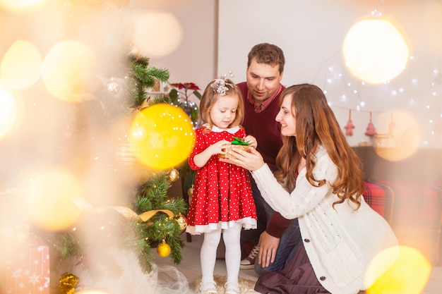 Familia feliz con hija abre el regalo en vacaciones de Navidad. Concepto de tiempo familiar