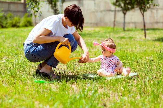 Familia feliz en el jardín. el agua de una regadera se vierte en las manos del niño. La madre le lava las manos a un niño en el jardín con una regadera amarilla.