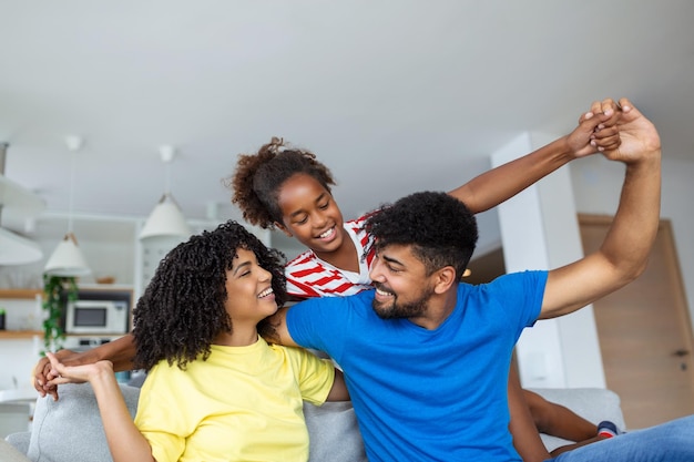 Família feliz joga juntos no sofá em casa, mãe, pai e filha, desfrutando de relaxamento feliz, passando tempo juntos na moderna sala de estar à noite