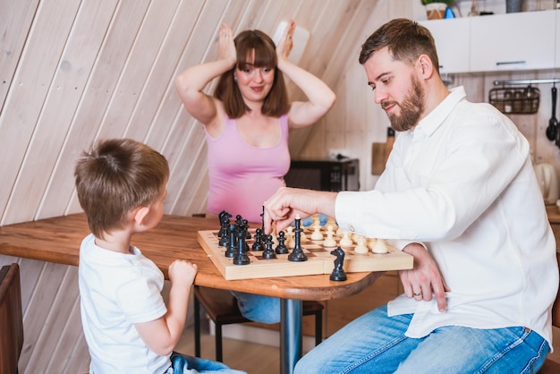 Família feliz jogando xadrez na cozinha