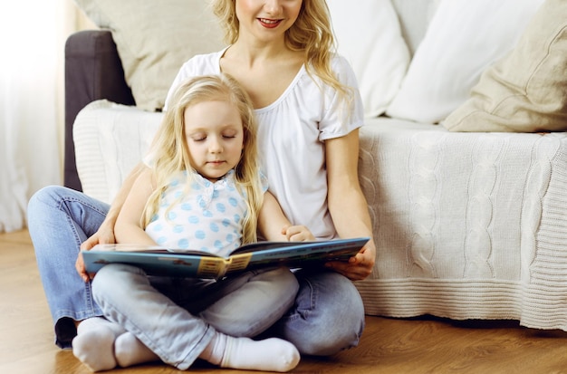Familia feliz. Joven madre rubia leyendo un libro a su linda hija mientras se sienta en el suelo de madera. concepto de maternidad
