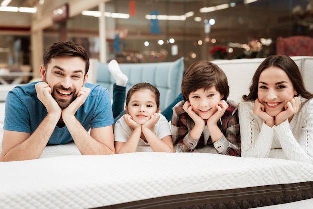 Familia feliz joven que se relaja en cama suave en tienda