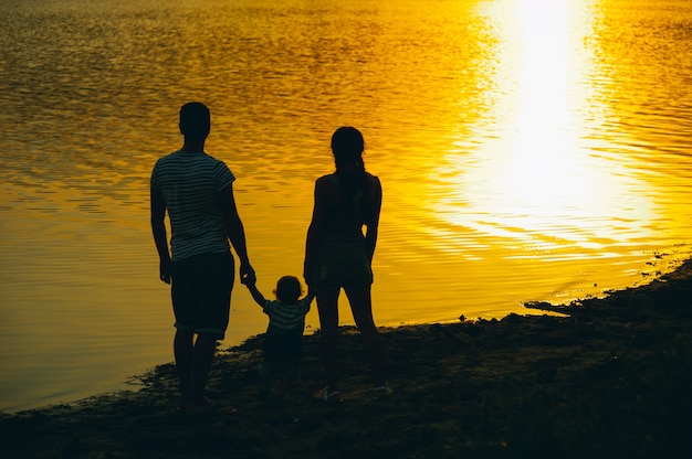 Familia feliz junto, padres con su pequeño hijo al atardecer. Padre levantando al bebé en el aire.