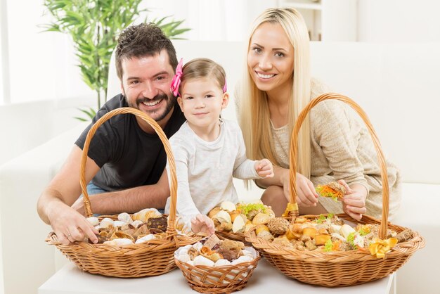 Familia feliz juntos, padres con hija sentada en el sofá en la sala de estar frente a cestas tejidas llenas de pastelería.